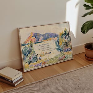 Puede incluir: Una pintura de acuarela enmarcada que representa una escena junto al lago con monta&ntilde;as y &aacute;rboles. La obra de arte presenta una cita en texto negro. La pintura se exhibe en un piso de madera junto a una pila de libros.