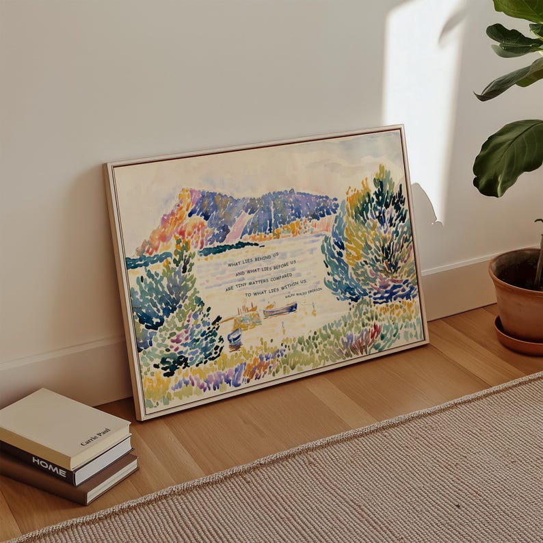 Puede incluir: Una pintura de acuarela enmarcada que representa una escena junto al lago con monta&ntilde;as y &aacute;rboles. La obra de arte presenta una cita en texto negro. La pintura se exhibe en un piso de madera junto a una pila de libros.