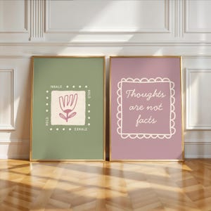May include: Two framed art prints. One print has a sage green background with a floral design and the words "INHALE, HOLD, EXHALE". The other print has a mauve background with the words "Thoughts are not facts". Both are in gold frames.