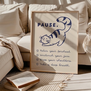 May include: A framed print featuring the word "PAUSE" in navy blue, accompanied by a cartoon cat illustration. The print includes instructions: "Relax your forehead," "Unclench your jaw," "Drop your shoulders," and "Take a deep breath."