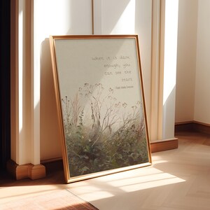 May include: A framed print with a gold-coloured frame. The artwork features a watercolour-style illustration of tall grasses and wildflowers. The text on the print reads, "When it is dark enough, you can see the stars." - Ralph Waldo Emerson.