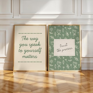 May include: Two framed art prints with gold frames. One print has the text "The way you speak to yourself matters" in green on a cream background. The other print has the text "trust the process" on a green floral background.