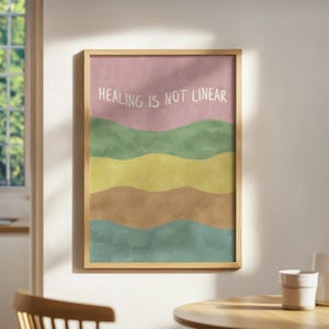 May include: A framed art print with a light wood frame. The artwork features a pastel color palette with horizontal bands of pink, green, yellow, brown, and teal. The text "HEALING IS NOT LINEAR" is written in white across the top.