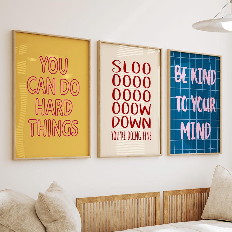 May include: Three framed art prints with motivational quotes. The first is yellow with red text saying "YOU CAN DO HARD THINGS." The second is off-white with red text saying "SLOO 0000 0000 000W DOWN YOU'RE DOING FINE." The third is blue with pink text saying "BE KIND TO YOUR MIND."