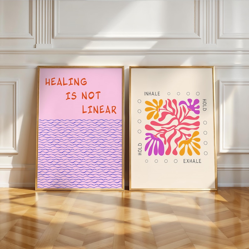 May include: Two framed art prints. One has the text "HEALING IS NOT LINEAR" in orange on a pink background above a wavy purple design. The other print says "INHALE HOLD EXHALE" with a floral design in orange, pink, and purple.