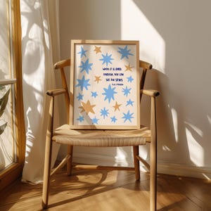 May include: A framed art print featuring a beige background with blue and gold star illustrations. The print includes the quote "When it is dark enough, you can see the stars" by R.W. Emerson. The artwork is displayed on a wooden chair.