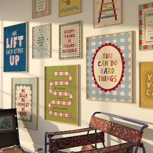 Op de afbeelding: Een galerijmuur met meerdere ingelijste posters met kleurrijke typografie en illustraties. De prints bevatten zinnen zoals 'We Lift Each Other Up', 'Everything Is Figureoutable', 'Progress Over Perfection' en 'You Can Do Hard Things'.