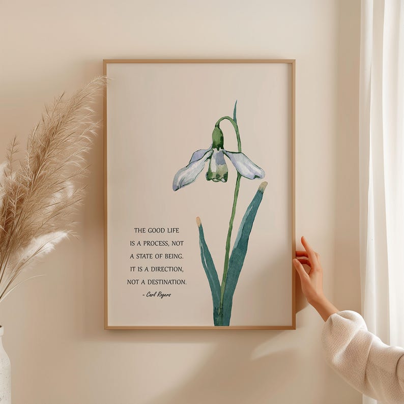 K&ouml;nnte beinhalten: Gerahmter Kunstdruck mit einer Aquarellillustration einer Schneegl&ouml;ckchenblume in Gr&uuml;n- und Wei&szlig;t&ouml;nen. Der Druck enth&auml;lt das Zitat "THE GOOD LIFE IS A PROCESS, NOT A STATE OF BEING. IT IS A DIRECTION, NOT A DESTINATION." von Carl Rogers.