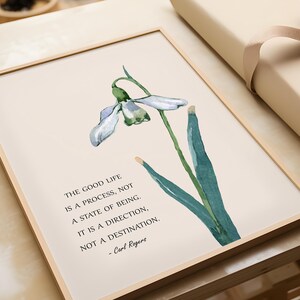 K&ouml;nnte beinhalten: Gerahmter Kunstdruck mit einer Aquarellillustration einer Schneegl&ouml;ckchenblume. Der Druck enth&auml;lt das Zitat "Das gute Leben ist ein Prozess, nicht ein Zustand des Seins" von Carl Rogers.