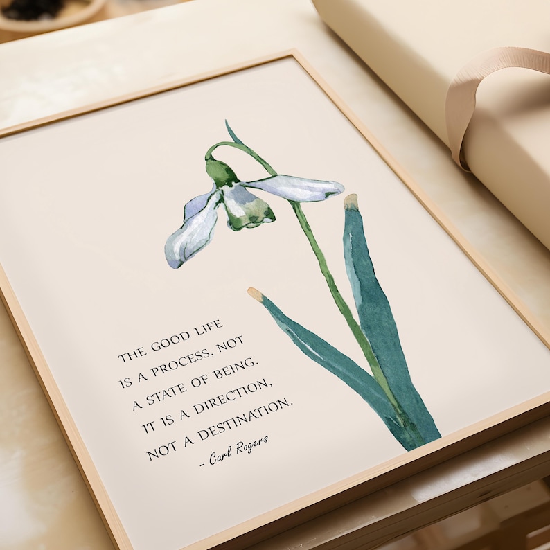 K&ouml;nnte beinhalten: Gerahmter Kunstdruck mit einer Aquarellillustration einer Schneegl&ouml;ckchenblume. Der Druck enth&auml;lt das Zitat "Das gute Leben ist ein Prozess, nicht ein Zustand des Seins" von Carl Rogers.