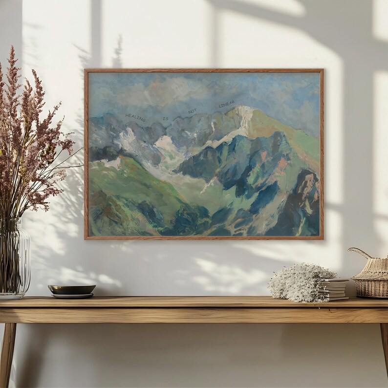 May include: A framed painting of a mountain range with a blue sky and white clouds. The text "Healing is not linear" is written across the top of the painting.