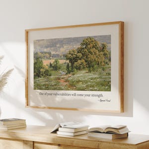 May include: A framed landscape art print with a light wood frame. The artwork depicts a field with trees and a quote that reads, "Out of your vulnerabilities will come your strength." - Sigmund Freud.
