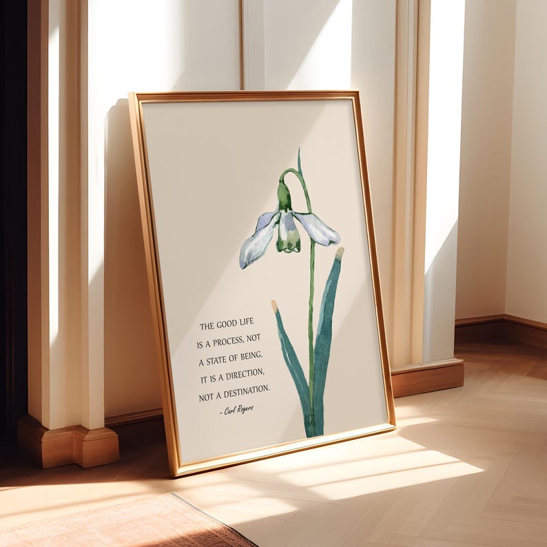 K&ouml;nnte beinhalten: Ein gerahmter Kunstdruck mit einer Aquarellillustration einer Schneegl&ouml;ckchenblume mit wei&szlig;en Bl&uuml;tenbl&auml;ttern und gr&uuml;nen Details. Der Druck enth&auml;lt das Zitat: "THE GOOD LIFE IS A PROCESS, NOT A STATE OF BEING. IT IS A DIRECTION, NOT A DESTINATION." in schwarzem Text.