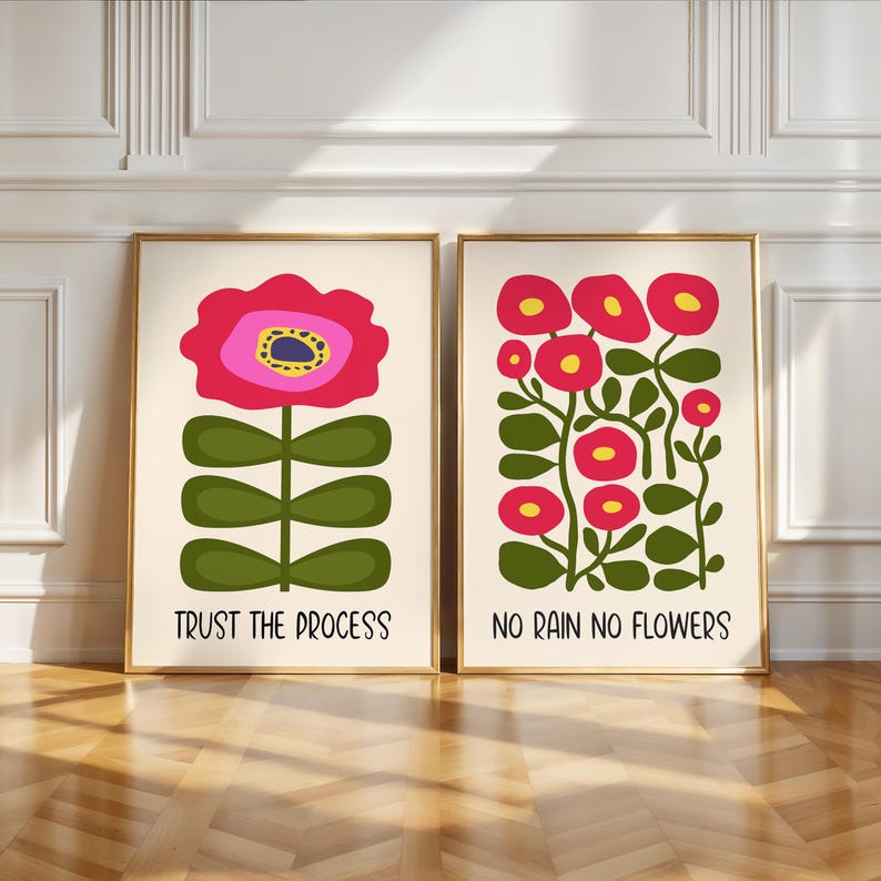 May include: Two framed art prints with gold frames. One print features a large pink flower with a yellow centre and the text "TRUST THE PROCESS". The other print displays red flowers with yellow centres and the text "NO RAIN NO FLOWERS".
