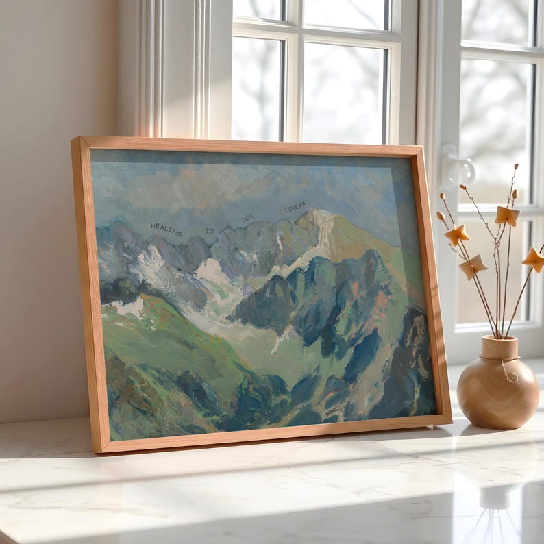 May include: A framed painting of a mountain range with a blue sky and white clouds. The text "Healing is not linear" is written across the mountains.