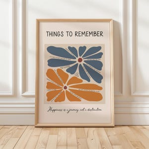 May include: A framed art print with the words "THINGS TO REMEMBER" at the top. The print features two large flower shapes in blue and orange, with inspirational text inside. The phrase "Happiness is a journey, not a destination" is at the bottom.