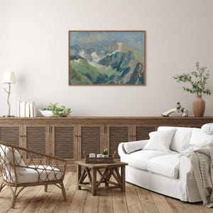 May include: A painting of a mountain range with snow-capped peaks and green valleys. The painting is framed in a light wood frame and hangs on a white wall.