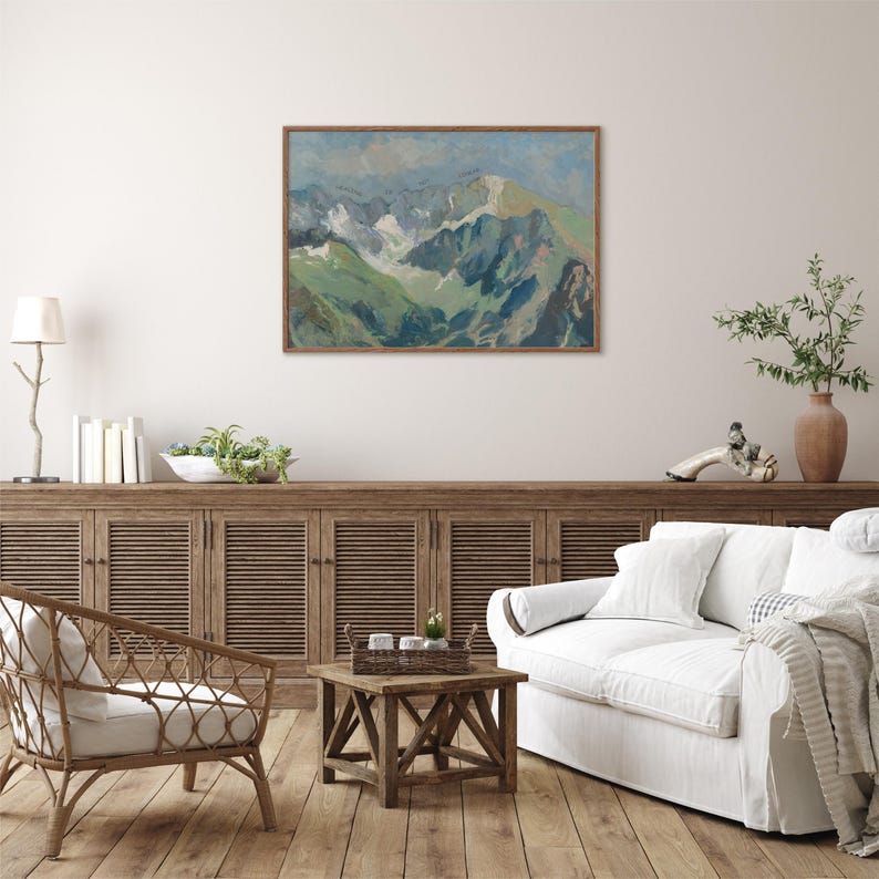 May include: A painting of a mountain range with snow-capped peaks and green valleys. The painting is framed in a light wood frame and hangs on a white wall.