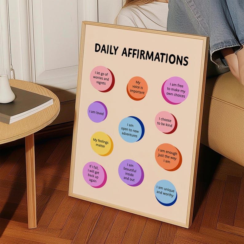 May include: A framed print with the words "DAILY AFFIRMATIONS" at the top. The print features colourful circles with positive affirmations such as "I am loved" and "I am unique and worthy". The frame is a light wood colour.