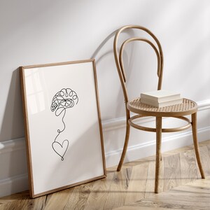 以下が含まれることがあります： 脳と心臓が描かれた白黒の線画。絵は薄い茶色の木製の額縁に収められ、薄い茶色の木製の椅子に立てかけられている。