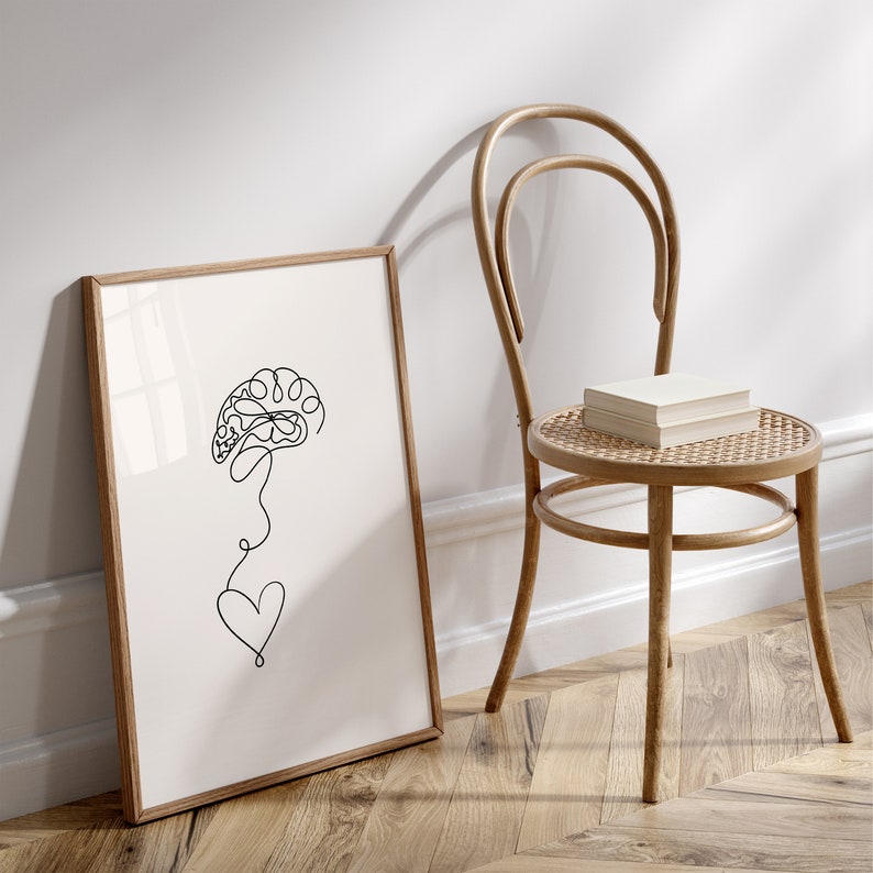 以下が含まれることがあります： 脳と心臓が描かれた白黒の線画。絵は薄い茶色の木製の額縁に収められ、薄い茶色の木製の椅子に立てかけられている。