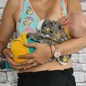 Könnte beinhalten: Ein Stilltop mit einem türkisfarbenen und rosa Vogel- und Schirmmuster. Das Baby trägt ein graues und gelbes Outfit mit einem Affenmuster. Am Handgelenk befindet sich eine goldene Uhr.
