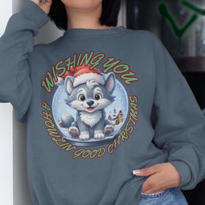 May include: A blue-grey sweatshirt featuring a cartoon wolf wearing a Santa hat inside a snow globe. The text reads "Wishing You A Howlin' Good Christmas" in red and green. The wolf is grey and white with a smiling face.