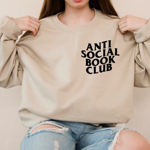 Puede incluir: Una sudadera beige con el texto "ANTI SOCIAL BOOK CLUB" impreso en negro en la parte delantera.