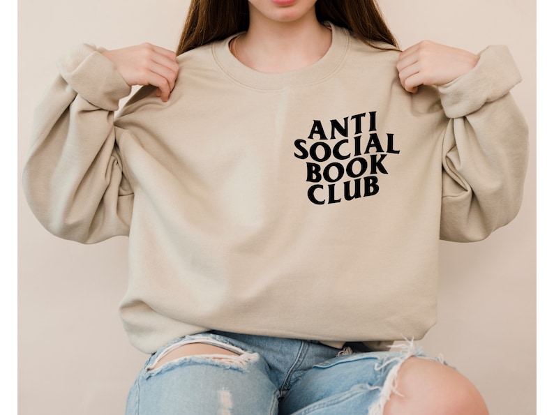 Puede incluir: Una sudadera beige con el texto "ANTI SOCIAL BOOK CLUB" impreso en negro en la parte delantera.