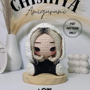 Könnte beinhalten: Handgefertigte Chishiya Amigurumi-Puppe mit weißer Kapuzenjacke und schwarzem Outfit. Die Puppe sitzt auf einem Holzsockel. Der Text "PDF PATTERN ONLY" und "LOW SEW!" sind ebenfalls sichtbar.