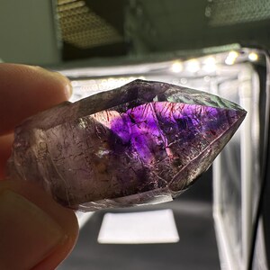 May include: A purple amethyst crystal point with a clear, glassy texture. The crystal has a double termination and is showing inclusions of other minerals.