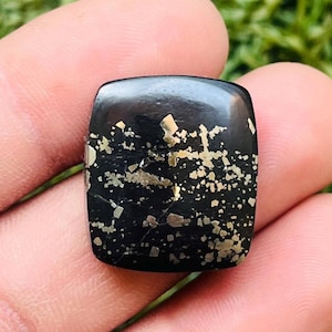 Pode incluir: Uma pedra preciosa preta de forma quadrada com manchas douradas.