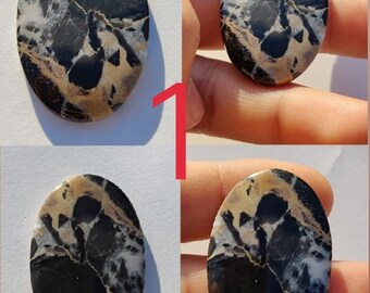 May include: A black, white, and gold oval cabochon gemstone with a swirling pattern. The gemstone is approximately 2 inches long and 1.5 inches wide.