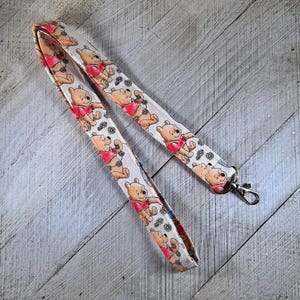 May include: A white lanyard with a repeating pattern of Winnie the Pooh characters in red, brown, and black. The lanyard has a silver metal clasp.