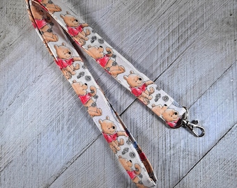 May include: A white lanyard with a repeating pattern of Winnie the Pooh characters in red, brown, and black. The lanyard has a silver metal clasp.
