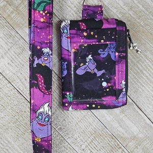 Puede incluir: Un conjunto de cord&oacute;n y funda para identificaci&oacute;n morados con un patr&oacute;n repetido de una bruja marina de dibujos animados sobre un fondo estrellado. La funda para identificaci&oacute;n tiene una ventana transparente y cierre de cremallera.