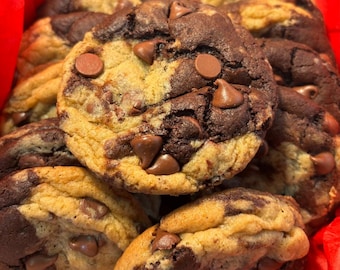 May include: A close-up of a group of chocolate chip cookies. The cookies are a mix of chocolate and vanilla dough, with chocolate chips throughout. The cookies are arranged in a red gift box.