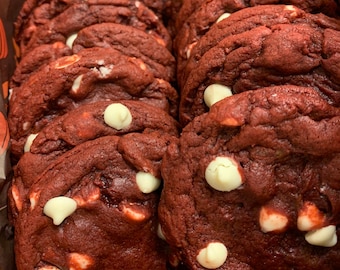 May include: A close-up of a box of red velvet cookies with white chocolate chips. The cookies are arranged in a stack and are surrounded by brown paper.