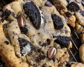 May include: Close-up of a chocolate chip cookie with Oreo cookie pieces, chocolate chips, and white chocolate chips. The cookie is on a wire rack.