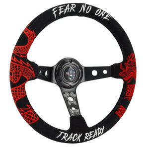 May include: Black steering wheel with red dragon embroidery and the text "FEAR NO ONE" and "TRACK READY". The wheel has a black center with a logo and decorative floral accents.