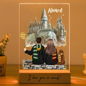 Könnte beinhalten: Ein personalisiertes LED-Nachtlicht mit einem Paar und einem Hund vor einer Burg, mit dem Text "Always!" und "I love you so much!" auf einem Holzsockel. Das Licht wird über ein Kabel mit Strom versorgt.