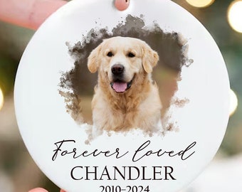 May include: A white ceramic Christmas ornament with a Golden Retriever's portrait inside a watercolour border. The text "Forever loved", the name "Chandler", and the years "2010-2024" are printed below the image. A beige ribbon is attached for hanging.
