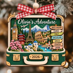 May include: A rectangular green suitcase-shaped ornament featuring the text Olivia's Adventure and 2026. The design includes landmarks like Big Ben, the Eiffel Tower, and the Colosseum, with a signpost listing countries and a red and white bow on top.