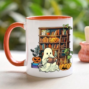May include: White ceramic coffee mug with an orange rim. The mug features a ghost reading a book in front of a bookshelf with pumpkins and a ladder. The text on the mug reads "Bookish Ghost".