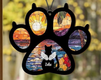 Può includere: Un ciondolo per finestra in vetro colorato a forma di impronta di zampa nera con un design a mosaico colorato. L'impronta di zampa presenta una silhouette di un gatto con le ali e il nome "Zeke" scritto sotto.