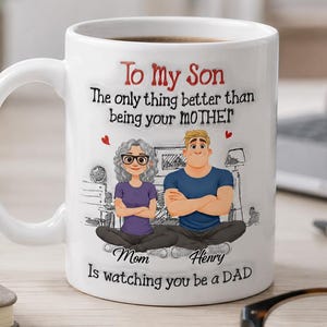 Op de afbeelding: Witte keramische mok met een handvat, met een afbeelding van een moeder en zoon. De tekst luidt "To My Son" en "The only thing better than being your MOTHER." Hieronder staat "Mom" en "Henry" en "Is watching you be a DAD."
