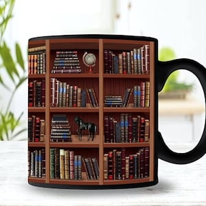Op de afbeelding: Zwarte keramische mok met een ontwerp van een boekenkast vol boeken. De boekenkast heeft een kleine globe op de bovenste plank en een zwart paardbeeldje op de derde plank.