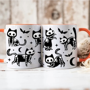 Pu&ograve; includere: Due tazze in ceramica bianca con bordi arancioni presentano un design a scheletro di gatto di Halloween in bianco e nero. Le tazze hanno un design a scheletro di gatto in bianco e nero con pipistrelli e mezze lune.