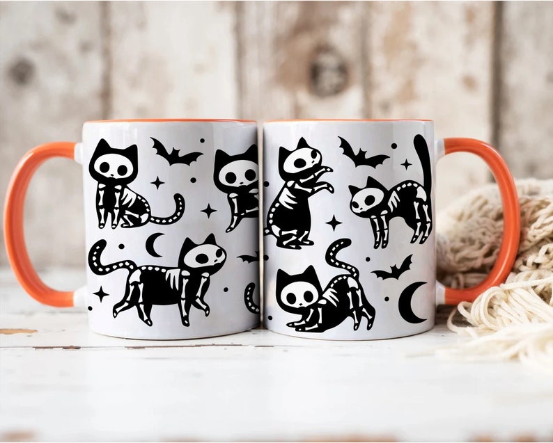 Pu&ograve; includere: Due tazze in ceramica bianca con bordi arancioni presentano un design a scheletro di gatto di Halloween in bianco e nero. Le tazze hanno un design a scheletro di gatto in bianco e nero con pipistrelli e mezze lune.