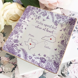 May include: Square ceramic dish with a floral and butterfly design in purple and gold. The dish has the text "Miles apart but close at heart" with a map of Texas and Kentucky, and the names "Mom" and "Kallie".